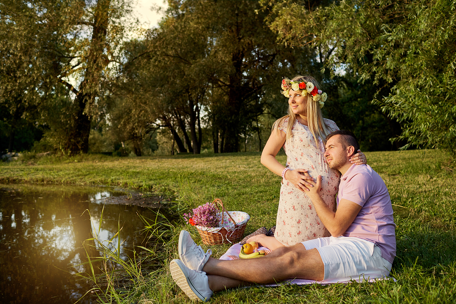 En mand og en dame sidder ved en sø, manden har hovedet på hans gravide kones mave