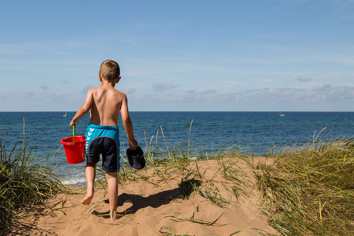 Dreng i badeshorts, der står og kigger ud over vandet