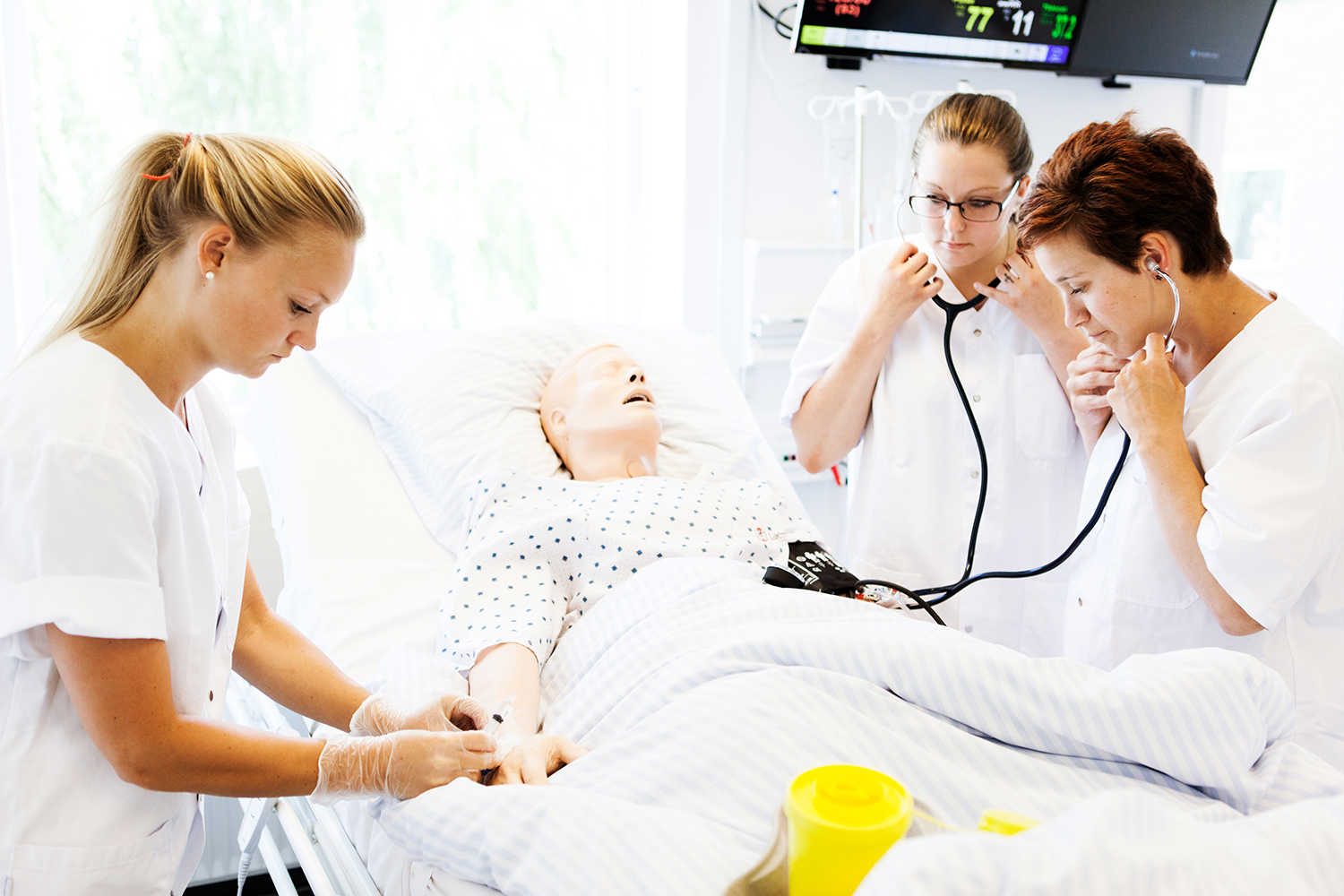 Tre social- og sundhedsassistenter øver sig på figurant i sengen